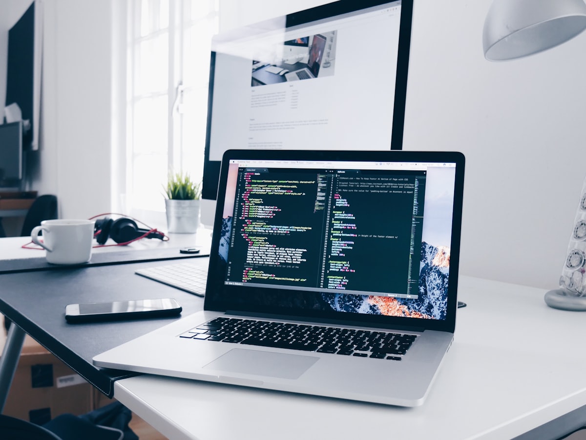 Developer at a desk with code on one monitor and the live site on another, warm natural light